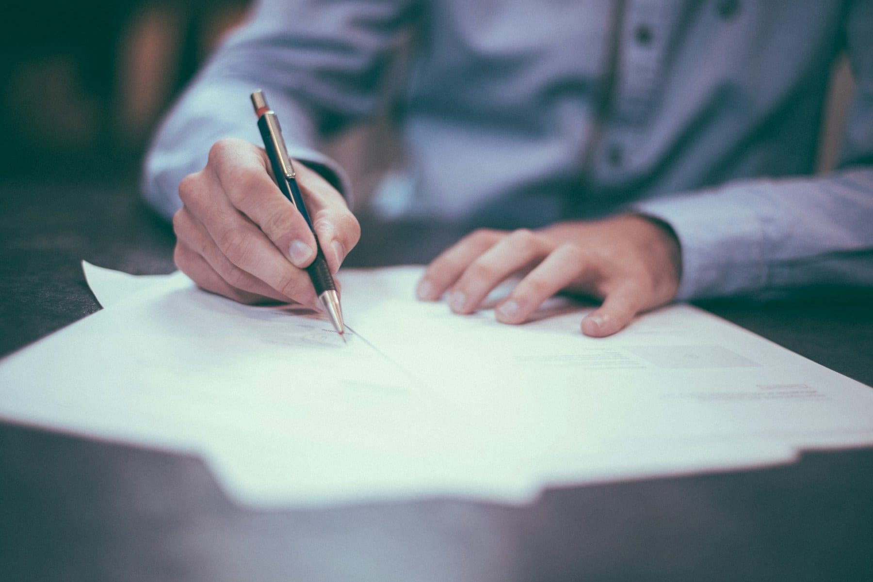 A hand signing a document at a desk.